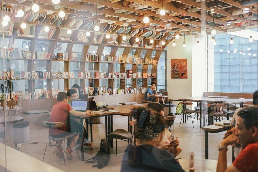 Không gian thư viện hiện đại với giá sách lớn, bàn ghế gỗ và nhiều người đang ngồi đọc hoặc làm việc.